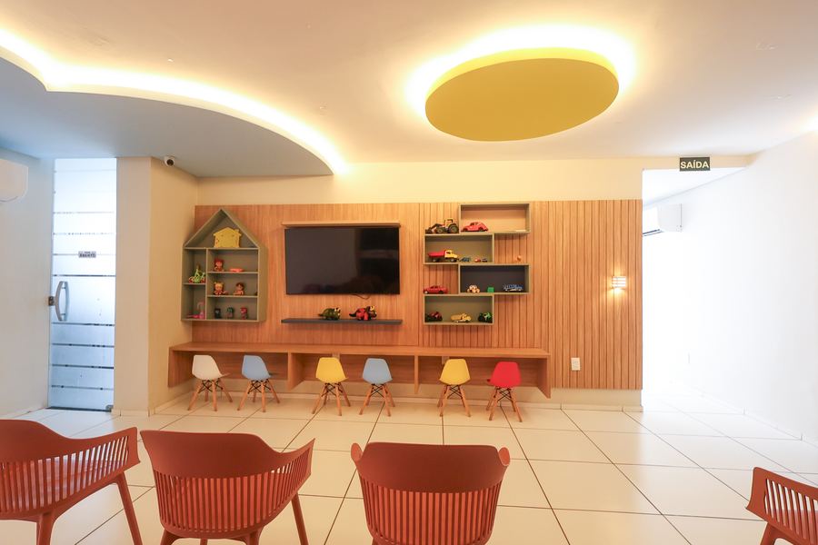 Ilha de espera com painel de TV, prateleiras em formato de casa e cadeirinhas infantis