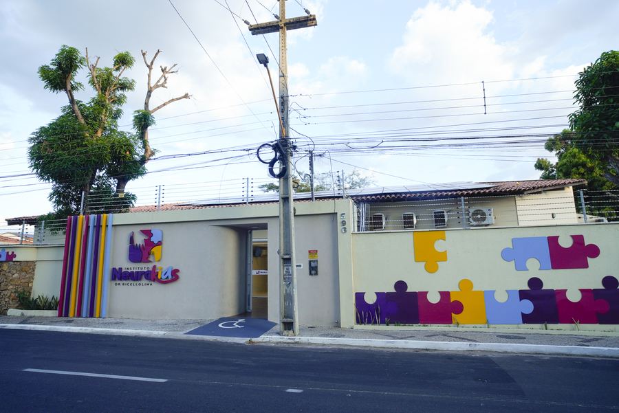 Vista da rua em frente ao Instituto NeuroKids, com muro de peças de quebra-cabeça