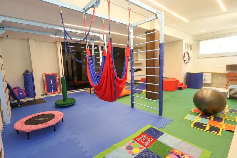 Sala de Terapia Ocupacional com balanços, parede de escalada e piso emborrachado colorido